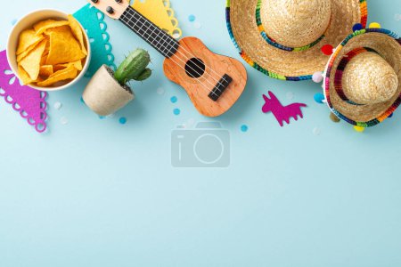 Festive Cinco de Mayo arrangement seen from the top view, including sombreros, a vihuela, cacti, flags, confetti, and a nacho bowl on a gentle blue background, space for copy