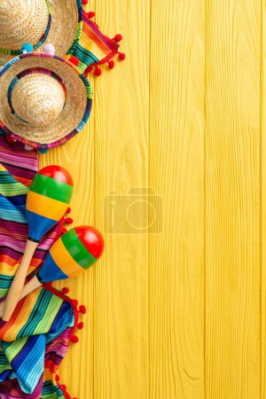 Colorful Cinco de Mayo vertical scene: top view of sombreros and maracas. Vibrant serape adorn the yellow wooden desk. Text-friendly space