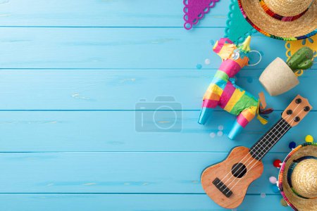 Embrace Cinco de Mayo vibes: top view of sombreros, vihuela, lama pinata, cactus, flag garland, confetti on wooden blue surface. Ideal for festive messaging