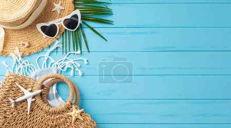 Strandurlaub Accessoires wie Strohhut, Sonnenbrille, Tasche und Palmblatt arrangiert auf einer lebendigen blauen Holzoberfläche, symbolisieren Sommerreise und Freizeit