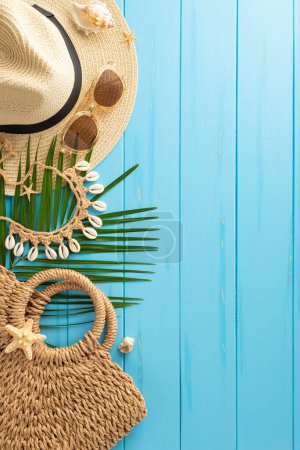 Téléchargez les photos : Le fond vertical en bois bleu met en valeur les éléments essentiels des vacances d'été : un chapeau de paille élégant, des lunettes de soleil assorties, un sac tissé et des feuilles de palmier tropical. Parfait pour les thèmes de voyage et de vacances - en image libre de droit