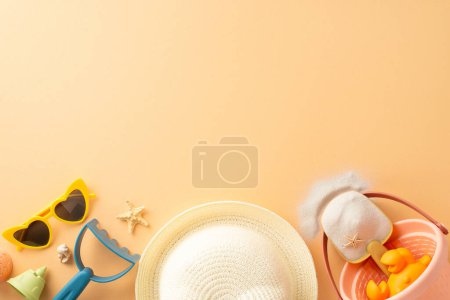 Overhead view of summer beach essentials spread out including sunglasses, sand toys, starfish, and a white beach hat on a sand-colored background