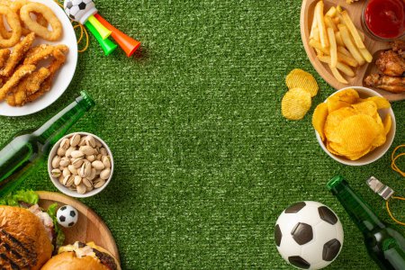 Téléchargez les photos : Une variété de collations de jour de jeu disposées sur un fond d'herbe verte avec des ballons de football, des boissons et des accessoires de ventilateur - en image libre de droit