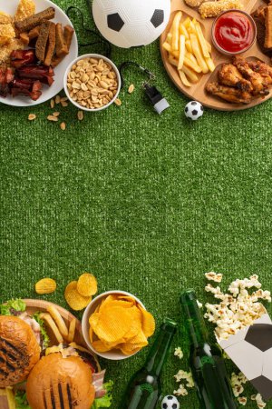 Eine Vielzahl von Snacks auf einem Gras vertikal strukturierten Hintergrund ideal für Fußballspieltag angeordnet. Neben einem Fußball gibt es Burger, Chips und Bier