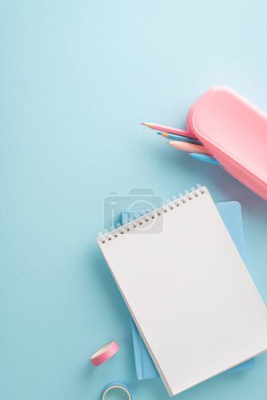 Ein vertikaler, sauber organisierter blauer Arbeitsbereich mit einem leeren Notizblock, rosa Mäppchen mit Buntstiften und Washi-Klebeband