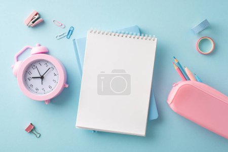 Un arrangement de fournitures scolaires comprenant une horloge rose, un bloc-notes et des crayons sur un fond bleu doux, transmettant un début d'activités scolaires rafraîchies et organisées