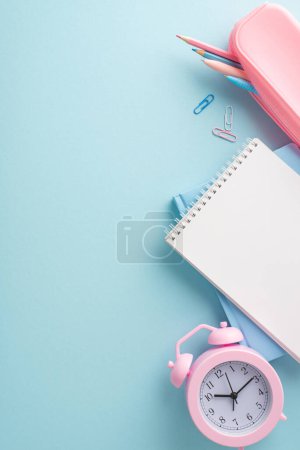A vertical minimalist vertical setup featuring school supplies, a pink alarm clock and notepad on a blue background, embodying a modern study space