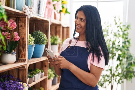 Photo for Middle age hispanic woman florist smiling confident using smartphone at florist - Royalty Free Image
