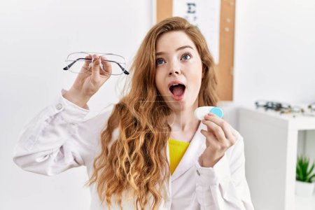 Photo for Young caucasian optician woman holding glasses and contact lenses at the clinic angry and mad screaming frustrated and furious, shouting with anger looking up. - Royalty Free Image