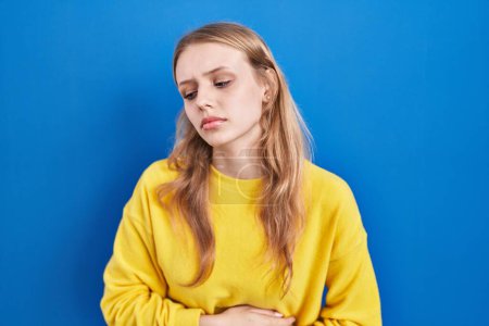 Photo for Young caucasian woman standing over blue background with hand on stomach because indigestion, painful illness feeling unwell. ache concept. - Royalty Free Image