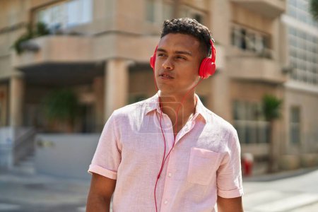 Téléchargez les photos : Jeune homme latin écoutant de la musique dans la rue - en image libre de droit