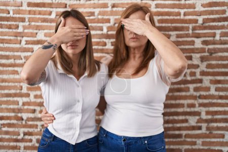 Photo for Hispanic mother and daughter wearing casual white t shirt covering eyes with hand, looking serious and sad. sightless, hiding and rejection concept - Royalty Free Image