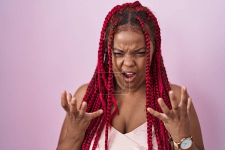 Photo for African american woman with braided hair standing over pink background crazy and mad shouting and yelling with aggressive expression and arms raised. frustration concept. - Royalty Free Image