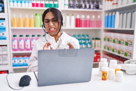 Téléchargez les photos : Jeune femme arabe travaillant à la pharmacie pharmacie en utilisant l'expression dégoûtée ordinateur portable, mécontent et craintif faire visage dégoût parce que réaction d'aversion. les mains levées - en image libre de droit