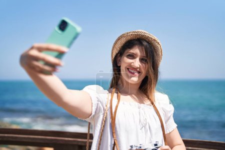 Young hispanic woman tourist smiling confident make selfie by smartphone at seaside
