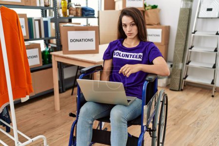 Photo for Young brunette woman as volunteer on donations stand sitting on wheelchair thinking attitude and sober expression looking self confident - Royalty Free Image