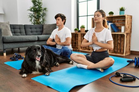 Téléchargez les photos : Jeune couple caucasien concentrer l'entraînement yoga avec chien à la maison. - en image libre de droit