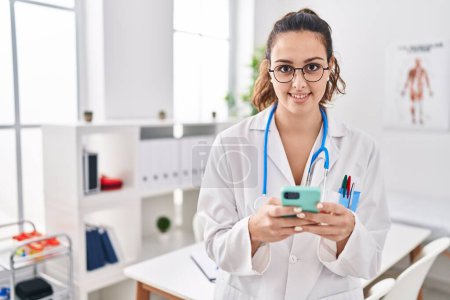 Photo for Young beautiful hispanic woman doctor smiling confident using smartphone at clinic - Royalty Free Image