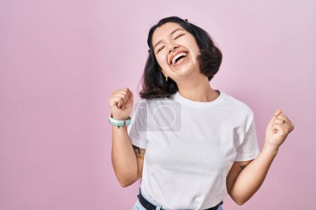 Photo for Young hispanic woman wearing casual white t shirt over pink background celebrating surprised and amazed for success with arms raised and eyes closed. winner concept. - Royalty Free Image