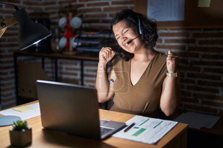 Photo for Young hispanic woman working at the office at night very happy and excited doing winner gesture with arms raised, smiling and screaming for success. celebration concept. - Royalty Free Image