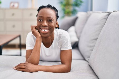 Foto de Mujer afroamericana sonriendo confiada acostada en el sofá en casa - Imagen libre de derechos