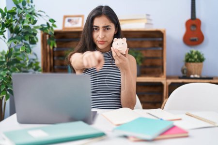 Photo for Young teenager girl studying using computer laptop pointing with finger to the camera and to you, confident gesture looking serious - Royalty Free Image