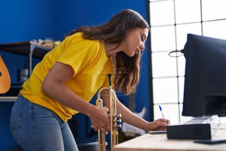 Téléchargez les photos : Young woman musician holding trumpet writing on notebook at music studio - en image libre de droit