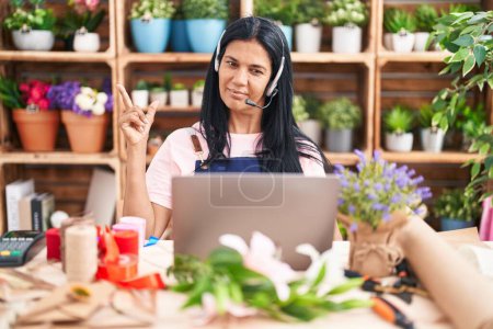 Photo for Mature hispanic woman working at florist shop doing video call smiling happy pointing with hand and finger to the side - Royalty Free Image
