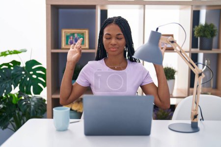 Photo for African american woman with braids using laptop at home relax and smiling with eyes closed doing meditation gesture with fingers. yoga concept. - Royalty Free Image