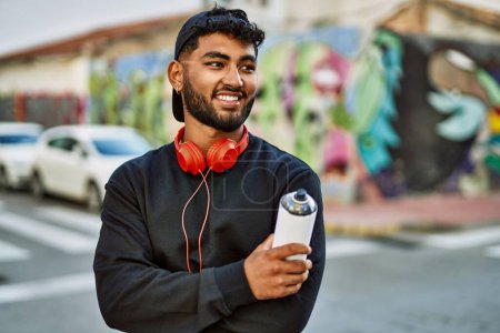 Téléchargez les photos : Jeune homme arabe souriant confiant tenant pulvérisation de graffiti dans la rue - en image libre de droit