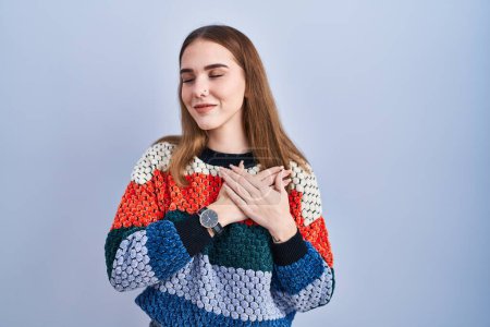 Téléchargez les photos : Young hispanic girl standing over blue background smiling with hands on chest with closed eyes and grateful gesture on face. health concept. - en image libre de droit