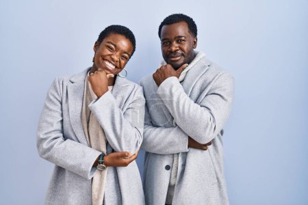 Photo for Young african american couple standing over blue background together looking confident at the camera smiling with crossed arms and hand raised on chin. thinking positive. - Royalty Free Image