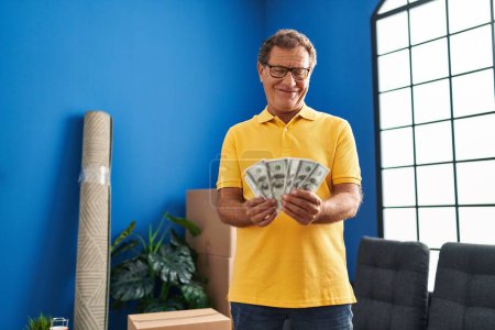 Photo for Middle age man smiing confident holding dollars at new home - Royalty Free Image