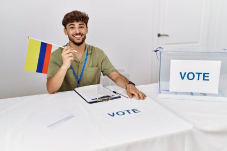 Téléchargez les photos : Jeune homme arabe souriant confiant tenant drapeau colombien travaillant au collège électoral - en image libre de droit