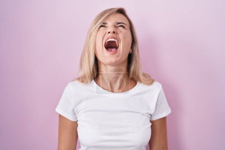 Téléchargez les photos : Jeune femme blonde debout sur fond rose en colère et folle hurlant frustrée et furieuse, criant de colère. rage et concept agressif. - en image libre de droit