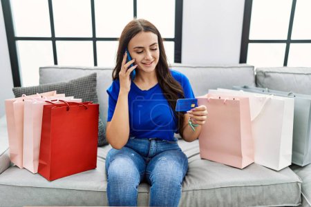Foto de Joven mujer caucásica comprando hablando en el teléfono inteligente con tarjeta de crédito en casa - Imagen libre de derechos