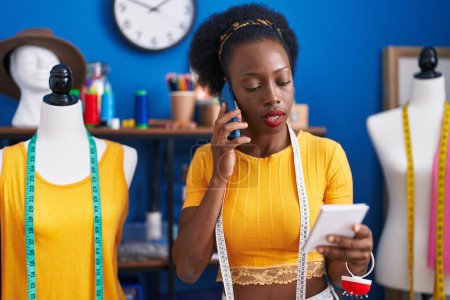 Téléchargez les photos : African american woman tailor talking on smartphone reading notebook at sewing studio - en image libre de droit