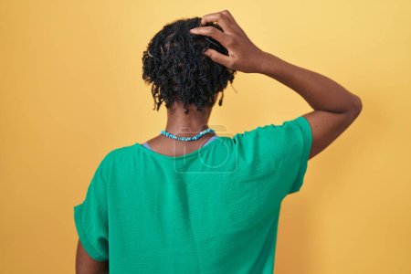 Foto de Mujer africana con rastas de pie sobre fondo amarillo hacia atrás pensando en la duda con la mano en la cabeza - Imagen libre de derechos