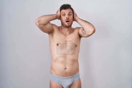 Photo for Young hispanic man standing shirtless wearing underware crazy and scared with hands on head, afraid and surprised of shock with open mouth - Royalty Free Image