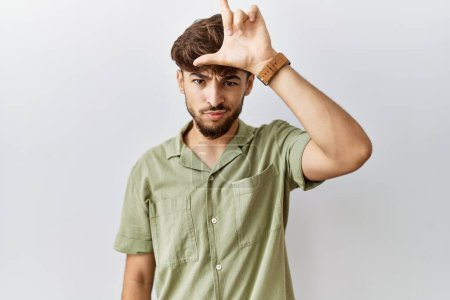 Photo for Young arab doctor man standing over isolated background making fun of people with fingers on forehead doing loser gesture mocking and insulting. - Royalty Free Image