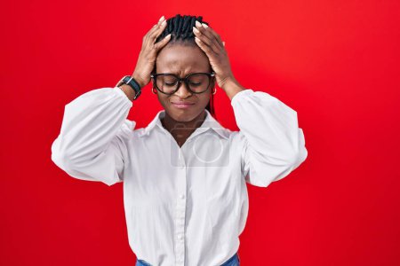 Foto de African woman with braids standing over red background suffering from headache desperate and stressed because pain and migraine. hands on head. - Imagen libre de derechos