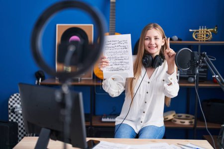 Téléchargez les photos : Young caucasian woman doing online music tutorial showing music sheet smiling with an idea or question pointing finger with happy face, number one - en image libre de droit