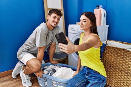 Foto de Hombre y mujer pareja lavando ropa haciendo selfie por el teléfono inteligente en la sala de lavandería - Imagen libre de derechos
