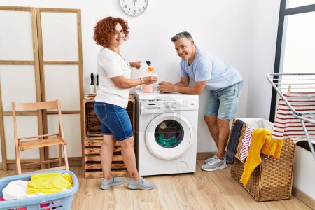 Foto de Hombre y mujer de mediana edad pareja vertiendo detergente lavando ropa en la lavandería - Imagen libre de derechos