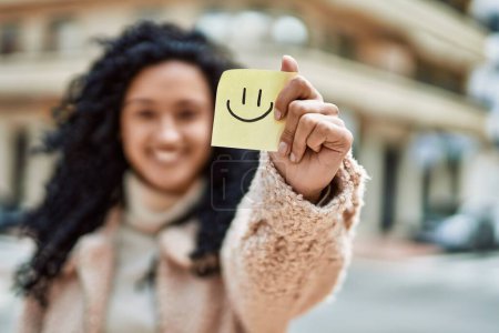 Photo for Young hispanic woman smiling confident holding smile reminder at street - Royalty Free Image