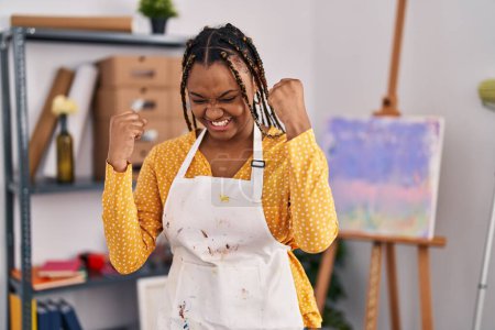Photo for African american woman with braids at art studio very happy and excited doing winner gesture with arms raised, smiling and screaming for success. celebration concept. - Royalty Free Image