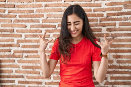 Téléchargez les photos : Young teenager girl standing over bricks wall shouting with crazy expression doing rock symbol with hands up. music star. heavy music concept. - en image libre de droit