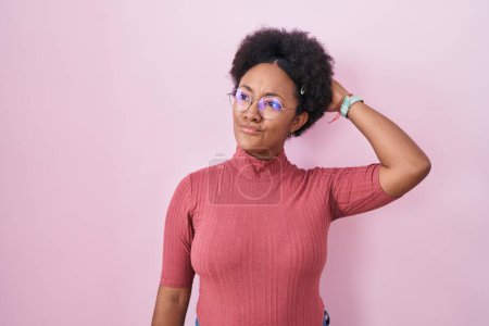 Photo for Beautiful african woman with curly hair standing over pink background confuse and wondering about question. uncertain with doubt, thinking with hand on head. pensive concept. - Royalty Free Image