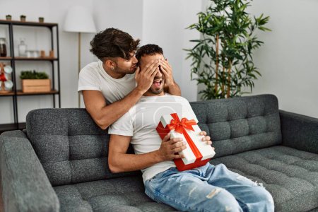 Téléchargez les photos : Deux hommes hispaniques couple surprise avec cadeau et mains sur les yeux à la maison - en image libre de droit