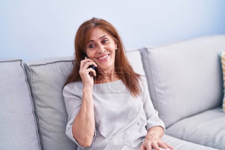 Photo for Middle age woman talking on the smartphone sitting on sofa at home - Royalty Free Image